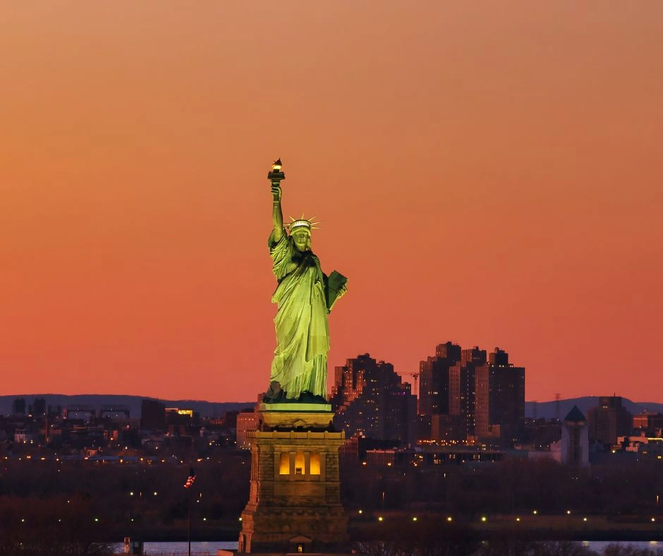 The Statue of Liberty standing tall at sunset with the New York City skyline in the background – a timeless symbol of freedom and a must-see landmark for first-time visitors.